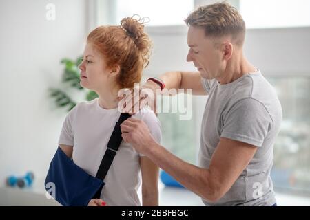 Physiothérapeute masculin examinant l'épaule d'une patiente avec une élingue pour bras Banque D'Images