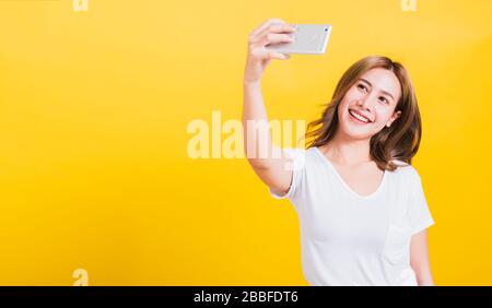 Portrait thaïlandais asiatique heureuse belle jeune femme souriante porter un t-shirt blanc faire des photos de selfie, appel vidéo sur smartphone regardant le téléphone, studi Banque D'Images