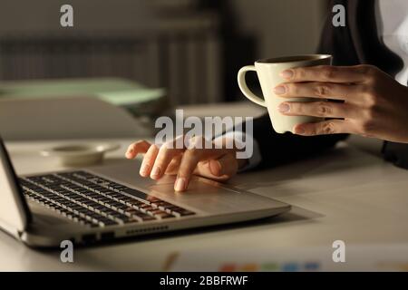 Gros plan sur les mains d'une femme d'affaires avec un ordinateur portable qui tient une tasse à café la nuit au bureau Banque D'Images