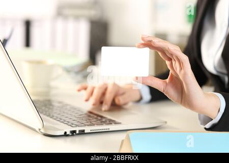 Gros plan de la main de la femme de direction avec ordinateur portable montrant une carte de crédit vierge à l'appareil photo sur adesk au bureau Banque D'Images