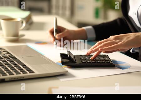 Gros plan sur les mains de la femme exécutive calculant avec calculatrice la nuit sur un bureau au bureau Banque D'Images