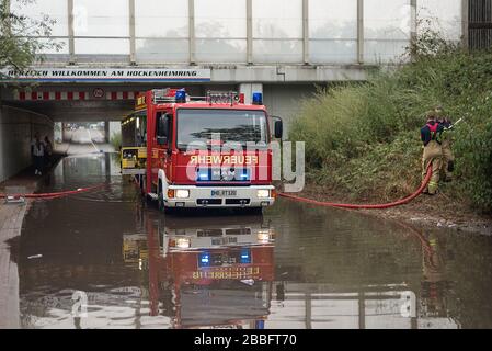 Deux pompiers d'urgence aident à pomper l'eau d'inondation d'une route avec leurs pompes puissantes de camions d'incendie rouges. Banque D'Images
