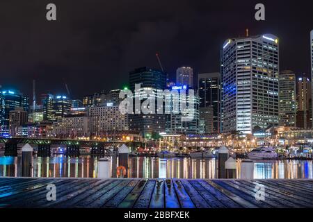 Quai en bois mouillé la nuit après la pluie à Sydney Darling Harbour, Nouvelle-Galles du Sud, Australie. Bâtiments modernes et bateaux le soir. Banque D'Images