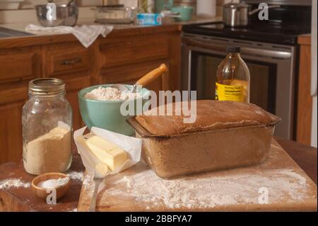 Pain Anadama dans la poêle en verre prêt à aller au four et les ingrédients sur le bloc de boucher et le comptoir dans la cuisine. Banque D'Images