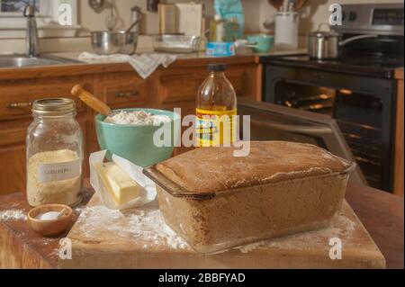 Pain Anadama dans la poêle en verre prêt à aller au four et les ingrédients sur le bloc de boucher et le comptoir dans la cuisine. Banque D'Images