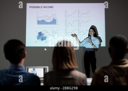 Jeune femme pointant vers l'écran de projection avec des variations graphiques et donnant un discours sur son propre projet de démarrage devant les investisseurs Banque D'Images
