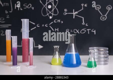 bureau de salle de classe avec flacons avec produits chimiques de couleur, instruments et un tableau noir dessiné avec l'enseignement des sciences en arrière-plan, l'enseignement des sciences chimiques Banque D'Images