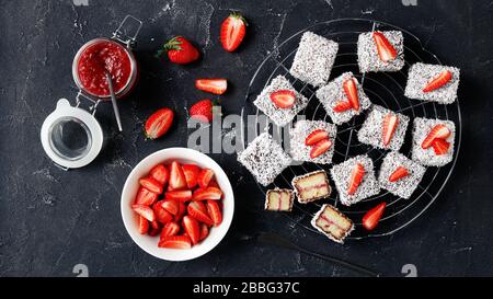 Lamingtons de dessert australien avec remplissage de confiture de fraises, enrobés de chocolat et de noix de coco râpée, servis sur un support en fil rond sur un b en béton foncé Banque D'Images