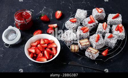 Dessert gastronomique australien : lamingtons avec remplissage de confiture de fraises, enrobés de chocolat et de noix de coco râpée, servis sur une grille ronde sur un dar Banque D'Images