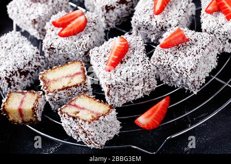 Lamelles sucrées : gâteau éponge carré avec couche de confiture de fraises, enrobé de chocolat et de noix de coco râpée déshydratée sur le dessus servi sur un ra à fil rond Banque D'Images