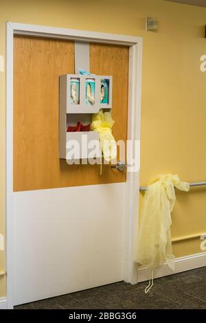 Indiana, États-Unis - 26 mars 2020: Gants et blouses de protection à l'extérieur de la porte de la chambre d'un patient dans un établissement médical. Banque D'Images