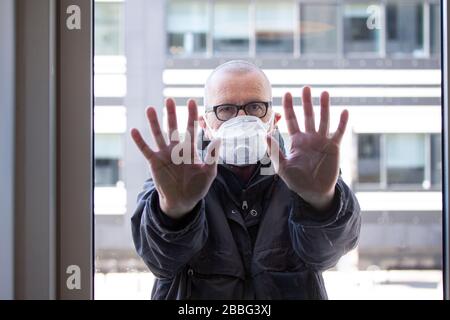 Homme avec masque de visage médical debout à l'extérieur d'une section de fenêtre avec ses mains enfoncées contre le verre de fenêtre et regardant à l'intérieur. Condition du virus Corona covid-19 Banque D'Images