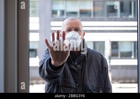 Homme avec masque de visage médical debout à l'extérieur d'une section de fenêtre avec sa main droite enfoncée contre le verre de fenêtre et regardant à l'intérieur. Corona covid-19 viru Banque D'Images