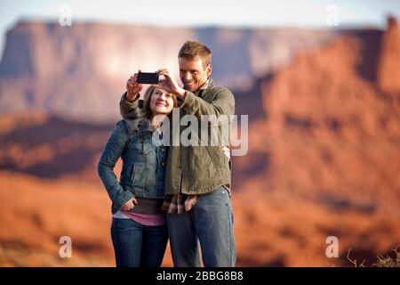 Un jeune couple souriant prenant un selfie avec un téléphone cellulaire avec un canyon du désert en arrière-plan Banque D'Images