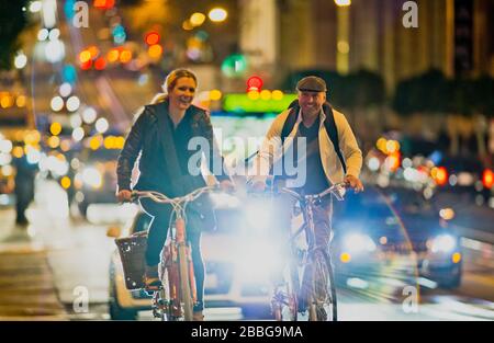 Homme mûr et jeune femme qui se rassemblent le long d'une rue animée de la ville la nuit Banque D'Images