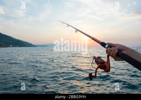 il y a un couple et ils pêchent pendant que le soleil est mis. Ils sont assis sur un échafaudage et l'un d'eux tient la canne de pêche contre le coucher du soleil. Banque D'Images