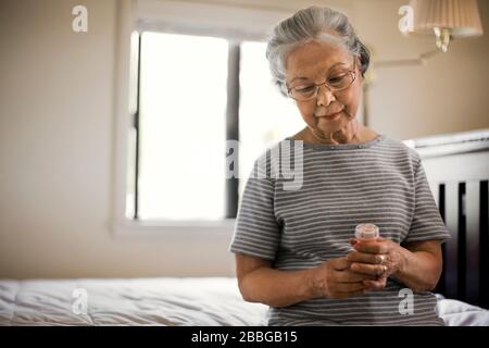 Femme senior assise sur son lit avec une bouteille de médecine. Banque D'Images