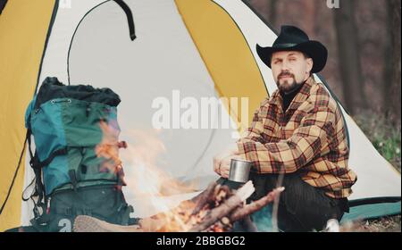Homme ayant du thé au feu de camp Banque D'Images