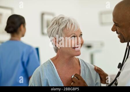 Une femme mûre et gaie ayant ses battements de cœur vérifiés par un médecin sympathique avec une infirmière en arrière-plan Banque D'Images