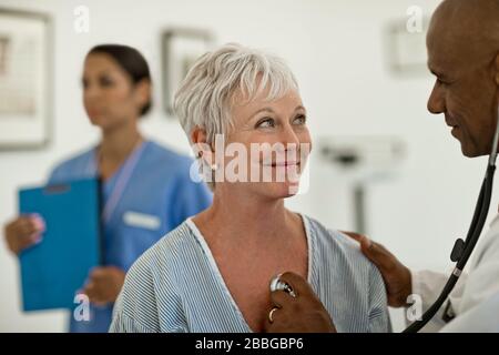 Femme mûre ayant son battement de coeur vérifié par son médecin avec l'infirmière en arrière-plan Banque D'Images