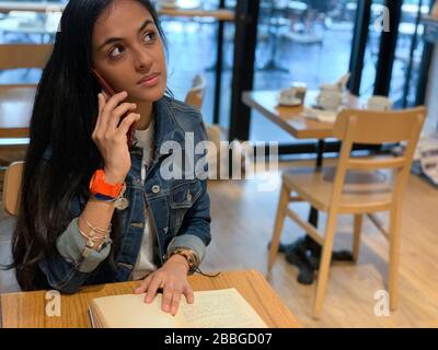 Jolie fille urbaine assise dans un café, lecture d'un livre et parler sur un téléphone mobile , Panama, Amérique centrale Banque D'Images