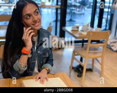 Jolie fille urbaine assise dans un café, lecture d'un livre et parler sur un téléphone mobile , Panama, Amérique centrale Banque D'Images