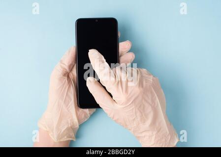 Microbes sur le concept de smartphone. POV haut en hauteur vue rapprochée photo des mains en gants écriture SMS SMS sur téléphone isolé fond bleu Banque D'Images