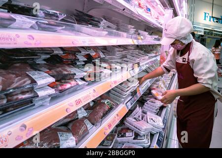 Bangkok, Thaïlande - 29 mars 2020 : une femme asiatique assistant de magasin portant un masque hygiénique pour le visage est en train de reconstituer la viande de porc et de poulet frais à gradins en super Banque D'Images