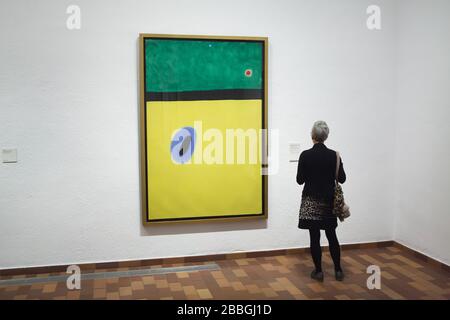 Visiteur devant la peinture par le peintre moderniste espagnol Joan Miró intitulé "l'aile du lark entourée de bleu doré rejoint le coeur du pavot dormant sur le pré clouté au diamant" (1967) exposé dans la Fundació Joan Miró (Fondation Joan Miró) à Barcelone, Catalogne, Espagne. Banque D'Images