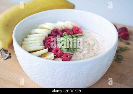 Petit déjeuner sain maison : porridge de flocons d'avoine avec banane, framboises mûres et graines de citrouille avec des ingrédients en arrière-plan Banque D'Images