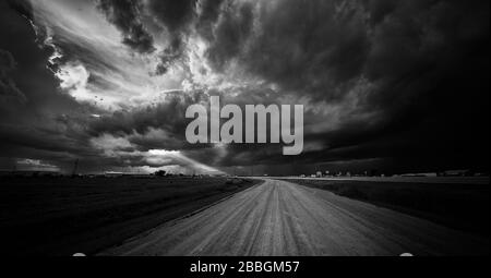 Tempête noire et blanche sur une route en gravier avec rayons du soleil qui brille dans le sud du Manitoba Canada Banque D'Images