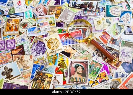 Une loupe et une pince à timbres sur le dessus d'une pile de timbres du monde entier. Banque D'Images