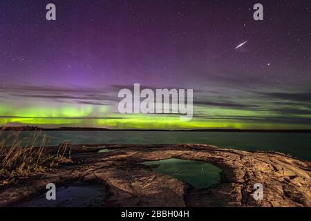 Aurora dansant et un météore parsemé sur le lac au Manitoba, le grand rocher du Canada dans la région d'eastman avec des lcouds ajoutant de la texture à un beau ciel Banque D'Images