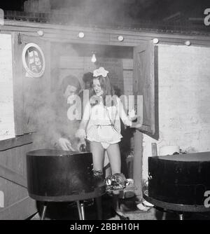 1973, historique, une jeune femme attrayante portant un fronceau de fête très court aidant à cuisiner dehors sur un grill à un barbecue de collecte de fonds au pub Lord Northbrook, Lee, sud-est de Londres, Angleterre. À l'angle de southbrook Rd, le pub est nommé d'après Lord Northbrook, dont la famille, Baring, la famille bancaire au 19e siècle avait un domaine dans l'arrondissement. Banque D'Images