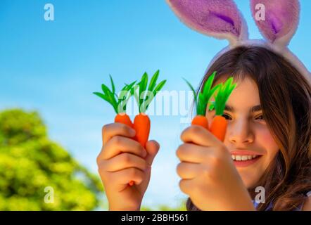 Portrait d'une jolie petite fille de lapin avec des carottes appréciant Pâques, ayant le jardinage amusant dans la cour une journée ensoleillée, la nourriture traditionnelle pour Pâques Banque D'Images