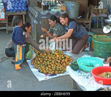 Acheter des fruits sur un marché en plein air à Luang Prabang, au Laos. Une femme lao, accompagnée d'une jeune fille, choisit des fruits d'une pile sur le sol avec l'aide d'une femme de vente souriante. La ville de Luang Prabang est classée au patrimoine mondial de l'UNESCO. Banque D'Images