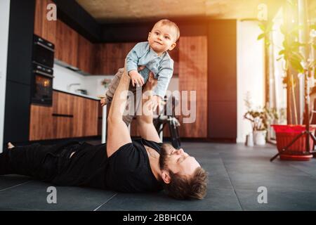 Joyeux père affectueux allongé sur un sol et soulevant son bébé