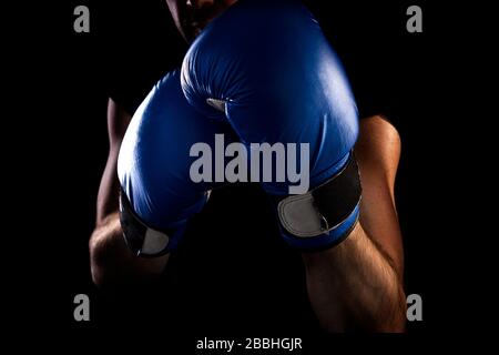 l'homme se tient en position de boxe, tient des gants de boxe bleus sur ses mains, fond sombre Banque D'Images