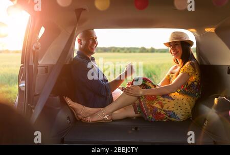 Couple amoureux assis dans un coffre de voiture et regarder le coucher du soleil Banque D'Images