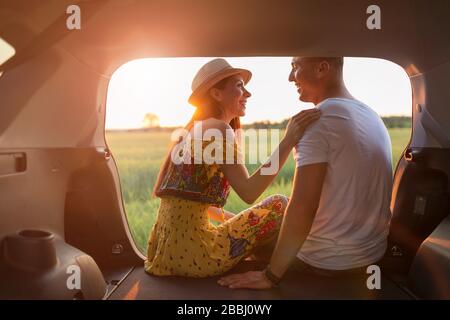 Couple amoureux assis dans un coffre de voiture et regarder le coucher du soleil Banque D'Images