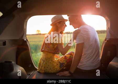 Couple amoureux assis dans un coffre de voiture et regarder le coucher du soleil Banque D'Images