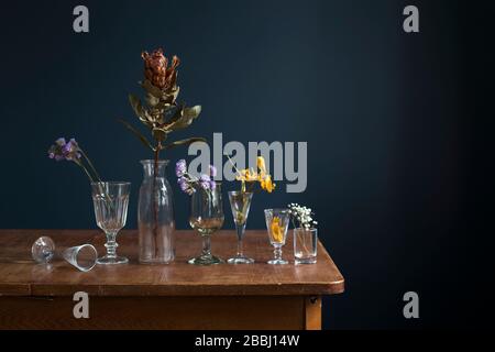 Fleurs séchées dans des verres en verre sur une table en bois face d'un mur bleu foncé. Carte d'art. Conception. Espace de copie. Banque D'Images