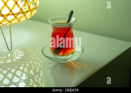 Thé turc traditionnel sur le plateau avec réflexion. Il y a une cuillère à l'intérieur du verre. C'est une boisson chaude et saine. Il y a un agneau élégant à côté Banque D'Images