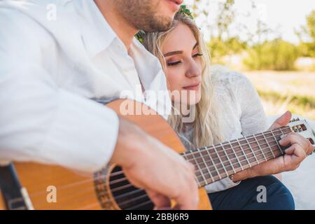 Un couple charmant passe du temps libre ensemble, date, bénéficie d'une atmosphère paisible en plein air dans les prairies. Le gars romantique joue de la guitare et chante des chansons à son Banque D'Images