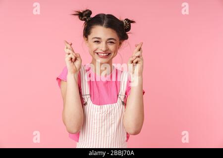 Photo de drôle fille avec anneau de nez tenant les doigts croisés pour la bonne chance et souriant isolé sur fond rose Banque D'Images