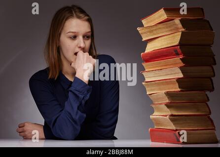 jeune fille et beaucoup de livres à côté d'elle. elle a un dur temps d'apprentissage Banque D'Images