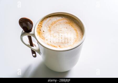 Café crémeux au lait dans une tasse blanche avec une cuillère. Banque D'Images