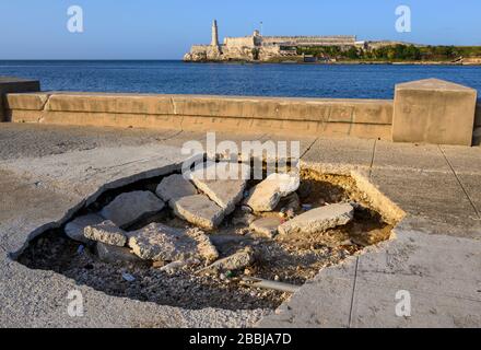 Trou dans le trottoir du Malecon, El Castillo de los Tres Reyes Magos del Morro ou simplement “El Morro” au loin, la Havane Vieja, Cuba Banque D'Images