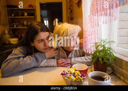 Une femme âgée regarde une fenêtre, avec sa petite-fille adulte, à la maison. Auto-isolation. Banque D'Images