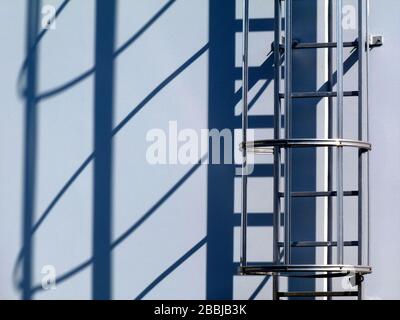 vue du détail de l'échelle d'accès au toit en aluminium. cage de sécurité. boulonnée au mur de béton blanc. longues ombres fortes en lumière du soleil vive. concept de construction. Banque D'Images